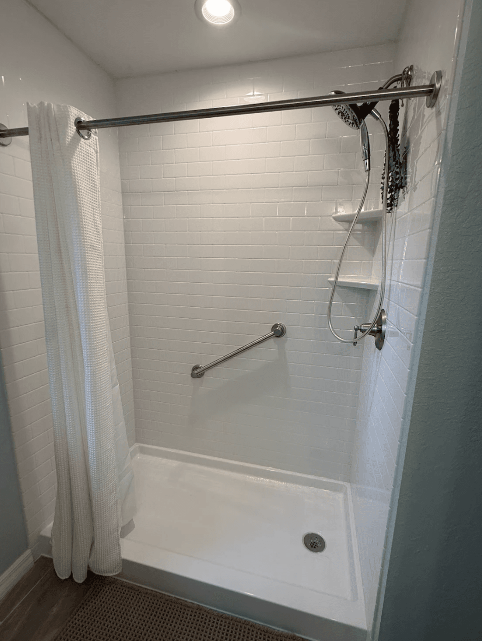 Completed tub-to-shower conversion with white wall surround and built-in corner shelves